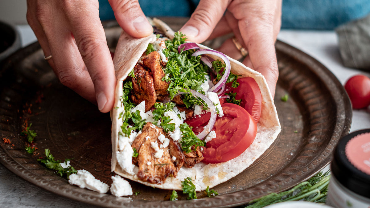 In den Händen halten sie ein Pita-Brot mit Fleisch, Feta, Tomaten, Zwiebeln und frischen Kräutern.