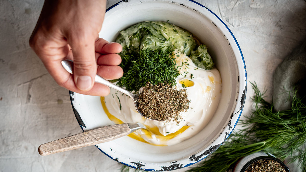 Joghurt mit geraspelter Gurke und frischem Dill, darüber streut man eine Handvoll getrockneter Kräuter.