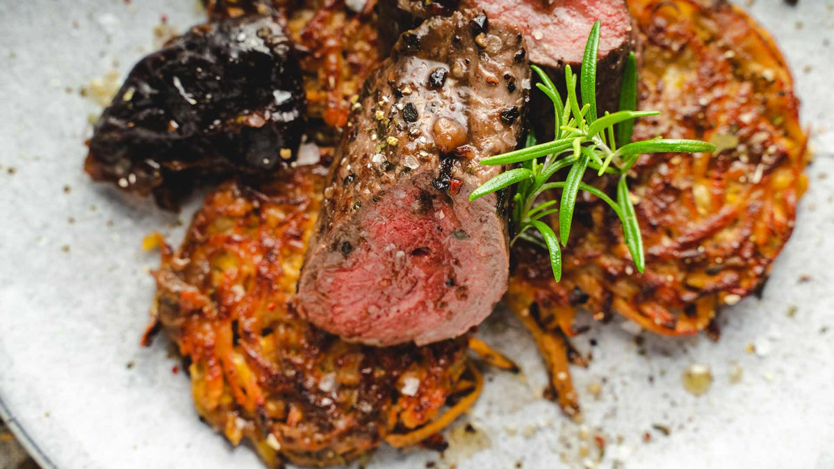 Geschnittenes Steak mit grobem Pfeffer auf Kartoffelpuffern, garniert mit frischem Rosmarin.