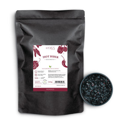 Schwarzer Beutel Isot Biber Chili neben einer Schale mit dunklen, aromatischen Chiliflocken.
