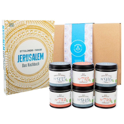 Fünf Gewürzgläser, braune Geschenkbox mit blauem Etikett, gelbes Muster im Hintergrund.