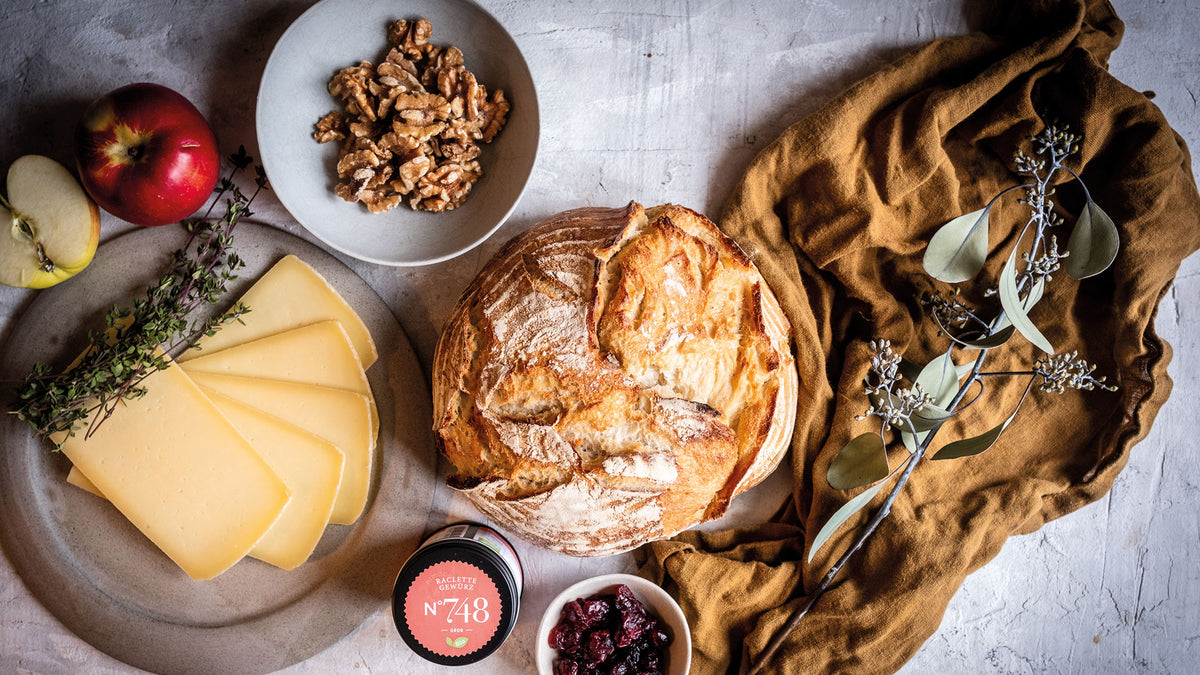 Sauerteigbrot, Käsescheiben, Apfel, Walnüsse und Cranberry-Marmelade auf einem braunen Tuch.