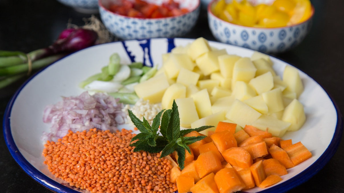Ein Teller mit gehackten Kartoffeln, Karotten, Sellerie, Knoblauch, roten Linsen, Schalotten und frischer Minze.