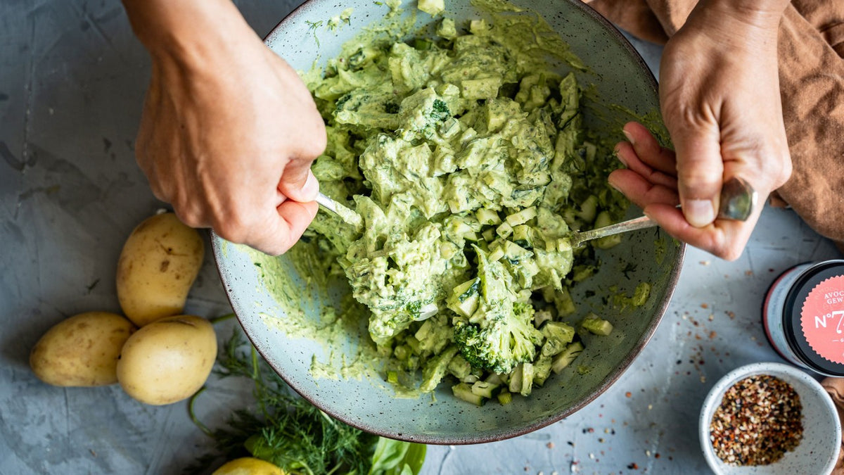 Mit den Händen den grünen, cremigen Salat in einer Schüssel vermengen, Kartoffeln und Gewürze auf den Tisch stellen.