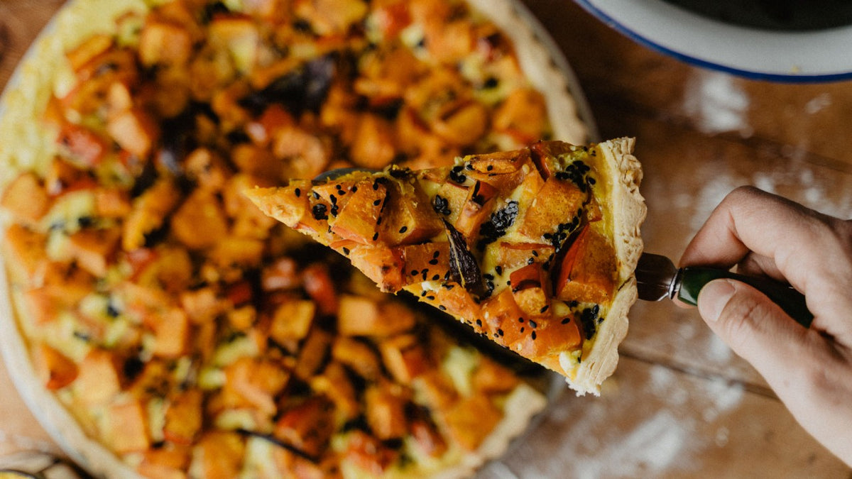 Eine Hand hebt ein Stück Gemüsepizza mit Käse von der gesamten Pizza auf einem Holztisch.