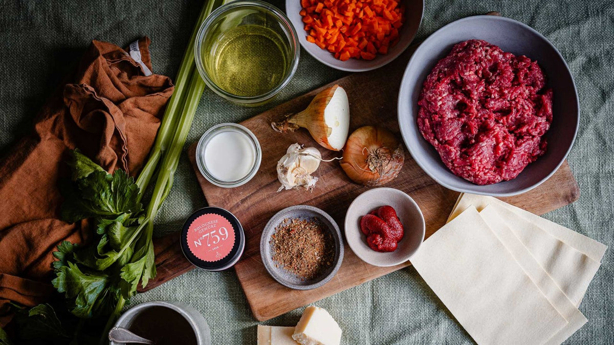 Hackfleisch, Lasagneplatten, Gemüse, Gewürze und Tomatenmark liegen auf einem Tisch.
