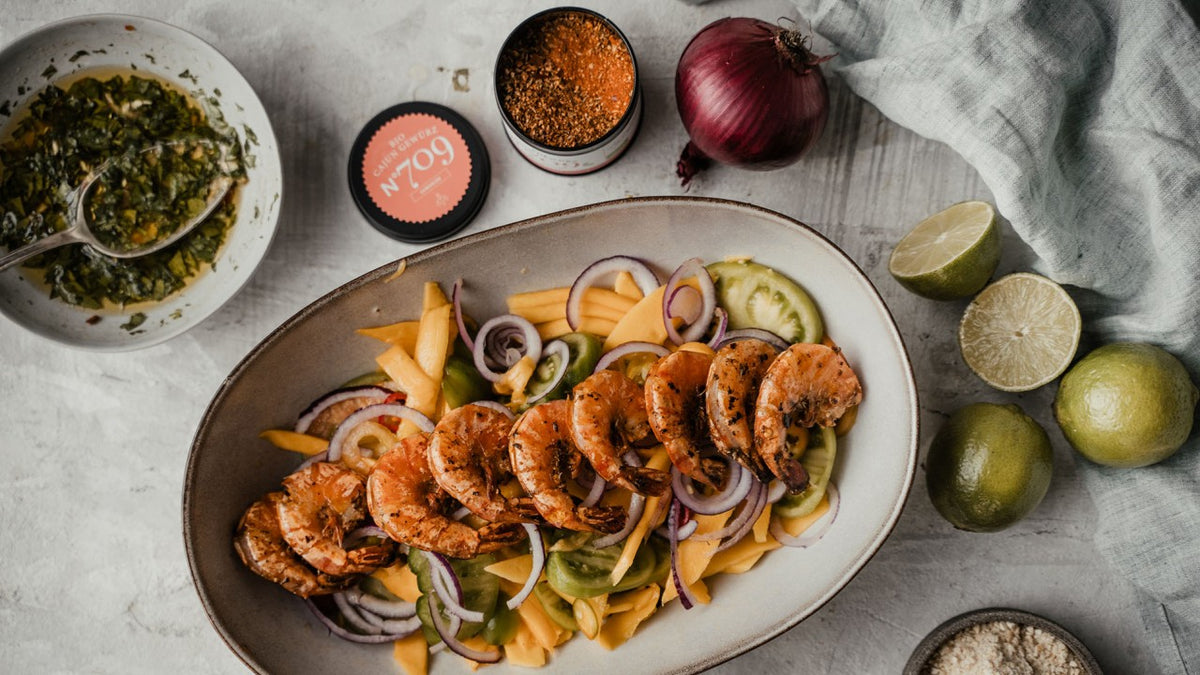 Gegrillter Garnelensalat mit Mango, Gurke und roten Zwiebeln auf einem bunten Teller.