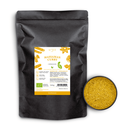 Eine Schale mit gelbem Currypulver steht neben einer schwarzen Tüte Bio Massaman Curry.