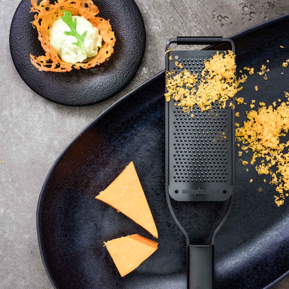 Geriebener Käse, zwei Käsescheiben und ein Käseknusper in einer Microplane Zesterreibe Black Sheep breit.