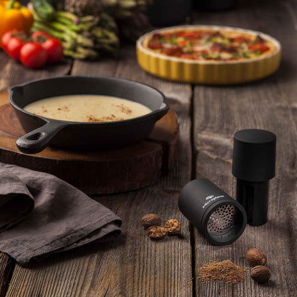Eine Pfanne Suppe, eine Microplane Muskatmühle 2 in 1 und ganze Muskatnüsse auf Holztisch.