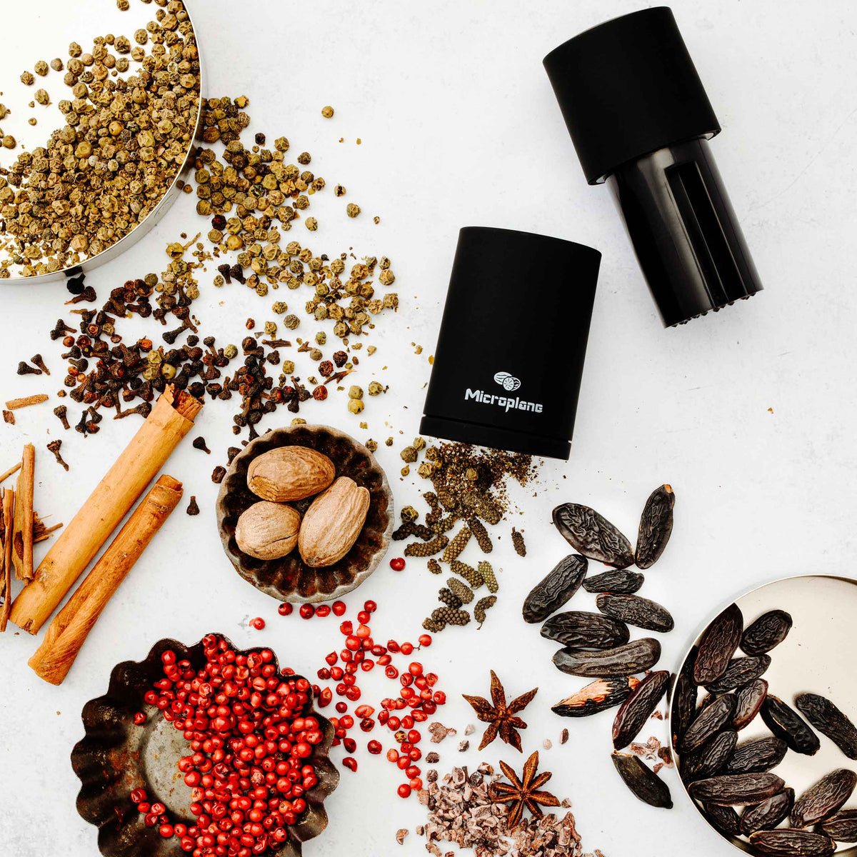 Verschiedene ganze und gemahlene Gewürze, zwei schwarze Mühlen und eine Microplane Muskatmühle.