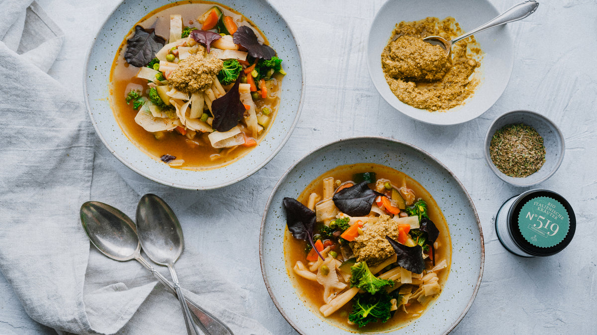 Zwei Schüsseln Gemüsesuppe mit Blattgemüse, daneben Grundausstattung 48 Gewürze und Löffel.