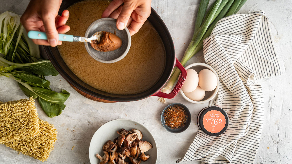 Gib das Miso in einen Topf mit Brühe, dazu die Ramen-Zutaten und ein gestreiftes Küchentuch.
