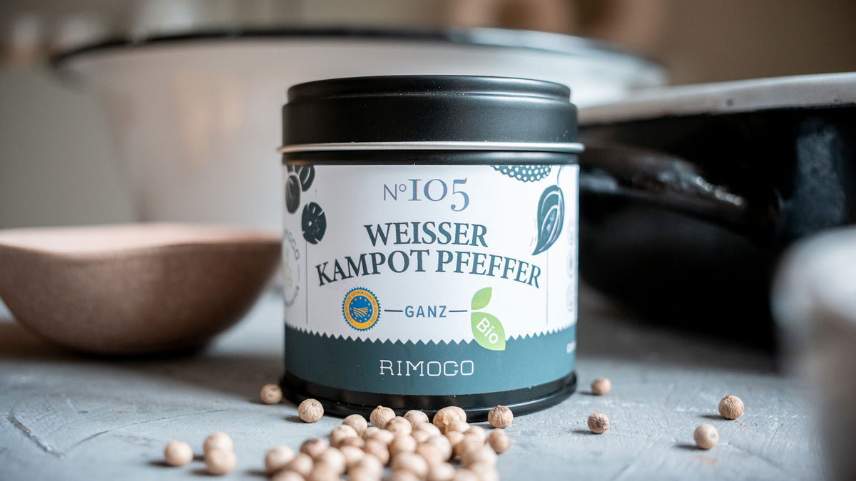 Rimoco Weisser Kampot-Pfeffer-Dose mit weißen Pfefferkörnern, die lose auf dem Tisch verstreut sind.
