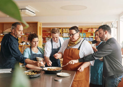 Sechs Personen kochen und servieren in einer hellen Küche.