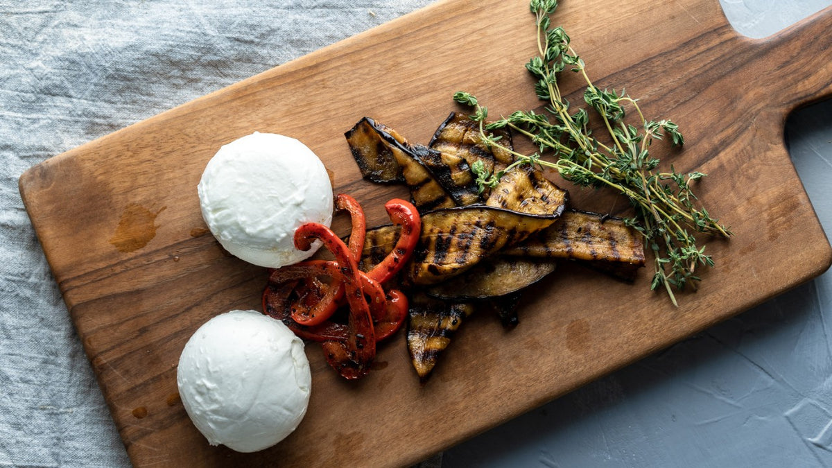 Mozzarellakugeln mit gegrillter Aubergine, roten Paprikastreifen und Thymian auf einem Holzbrett.