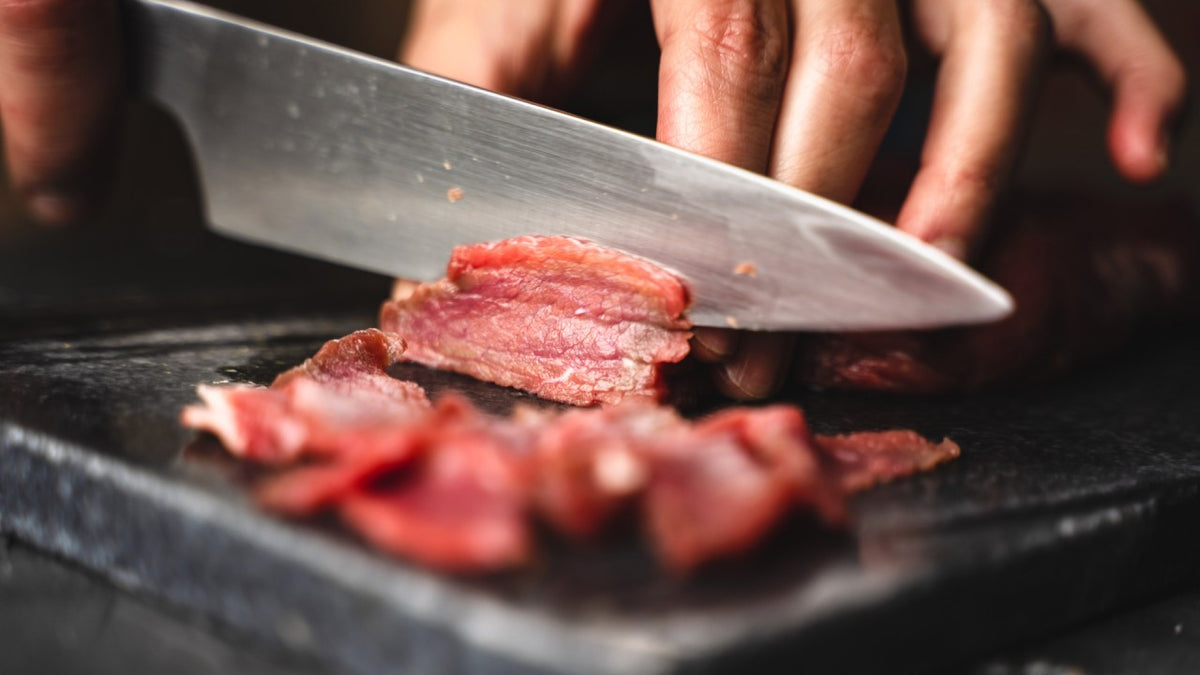 Schneiden Sie rohes Fleisch mit einem scharfen Messer auf einem dunklen Schneidebrett.