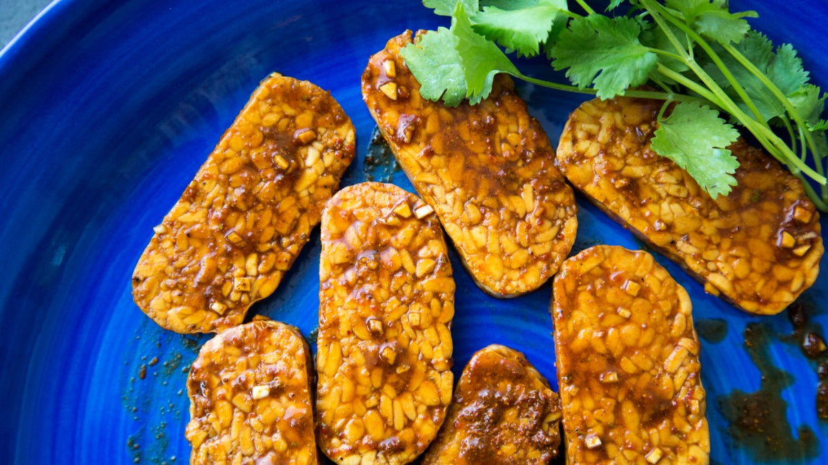 Rechteckige, marinierte Tempeh-Scheiben mit Koriander auf einem blauen Teller.
