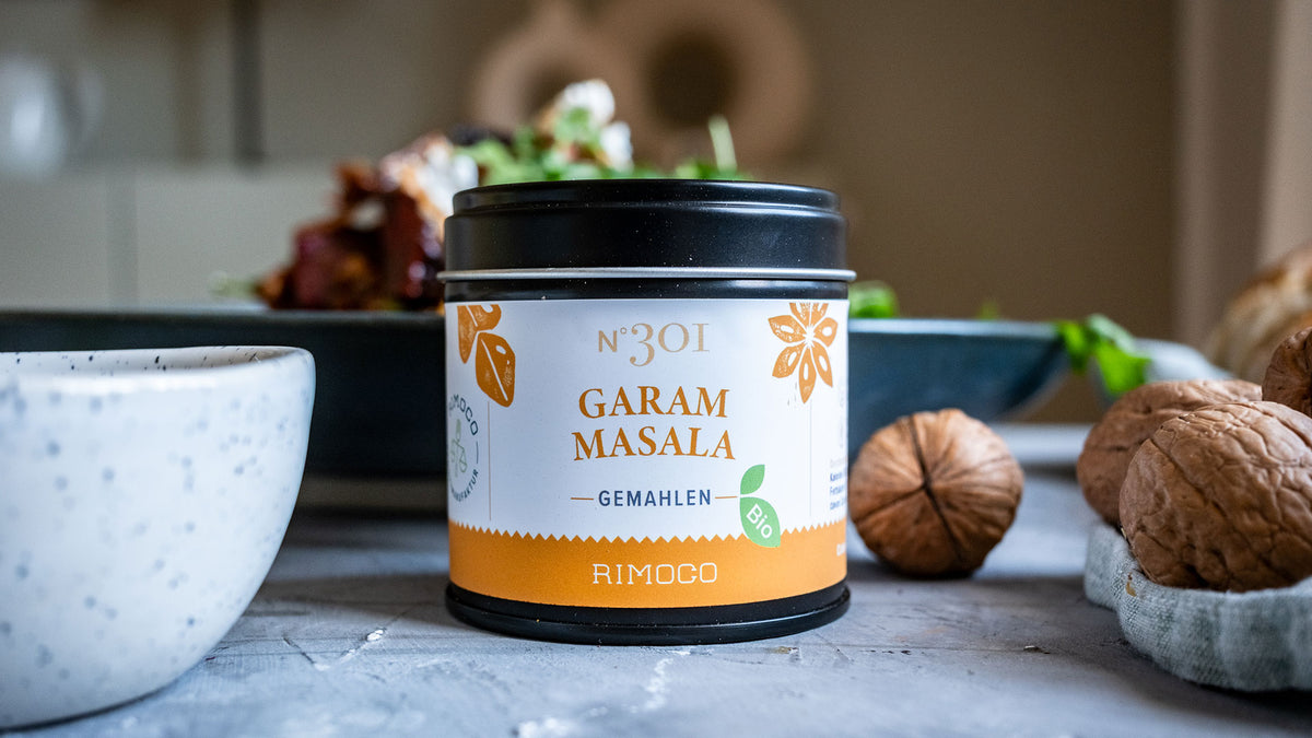 Ein Glas Rimoco Garam Masala auf einem Tisch, daneben Walnüsse und eine Schale.