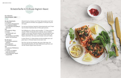Gebratener Lachs mit Kräutern, Zitronenscheiben, grünem Blattgemüse und rosa Pfefferkörnern.
