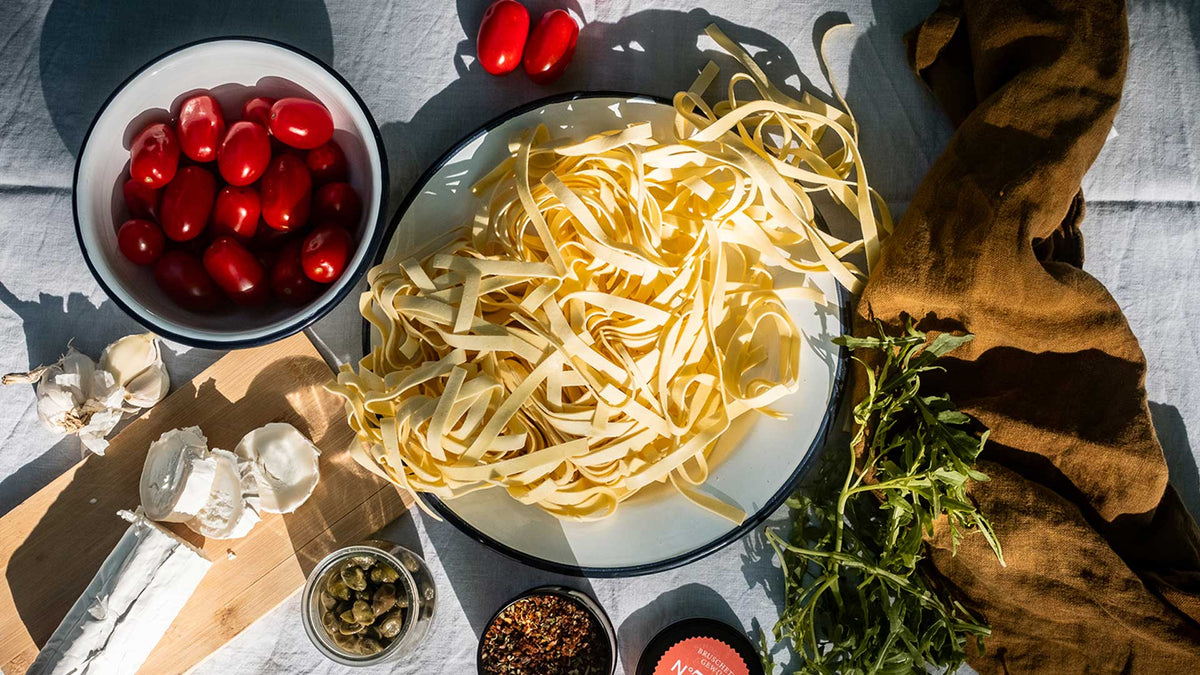 Tagliatelle mit Kirschtomaten, Ziegenkäse, Knoblauch, Kapern, Rucola und frischen Kräutern.