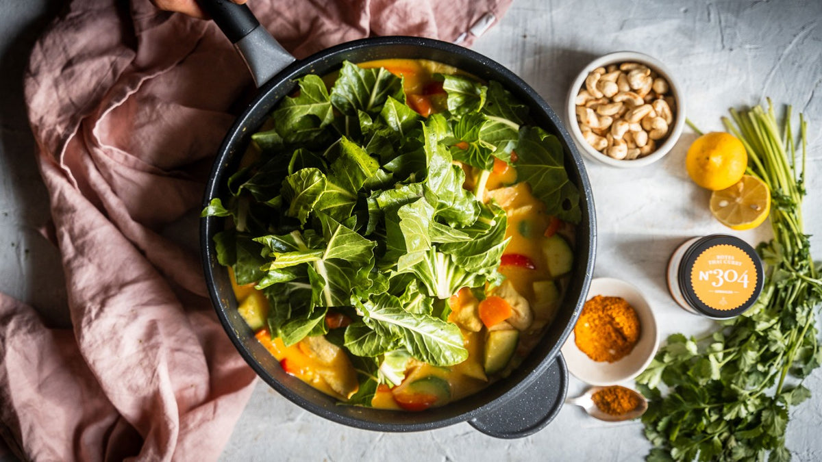 Veganes grünes Curry mit Gemüse, Cashewnüssen, Zitronenscheiben und frischen Kräutern aus der Pfanne.