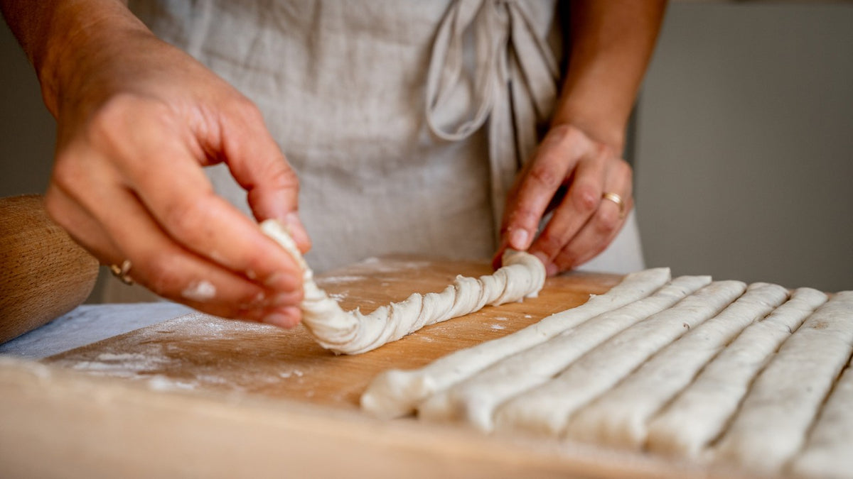 Auf einer bemehlten Fläche werden Teigstreifen ausgerollt, frische Pasta wird zubereitet.