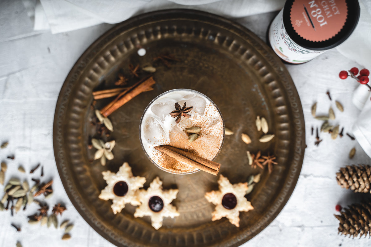 Eistee-Chai-Latte mit Zimtstange, Sternanis und Gewürzseminar Weihnachten auf Tablett mit Keksen.