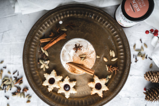 Eistee-Chai-Latte mit Zimtstange, Sternanis und Gewürzseminar Weihnachten auf Tablett mit Keksen.