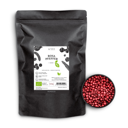 Bio Rosa Pfeffer in schwarzem Beutel neben einer Schale mit ganzen rosafarbenen Pfefferbeeren.