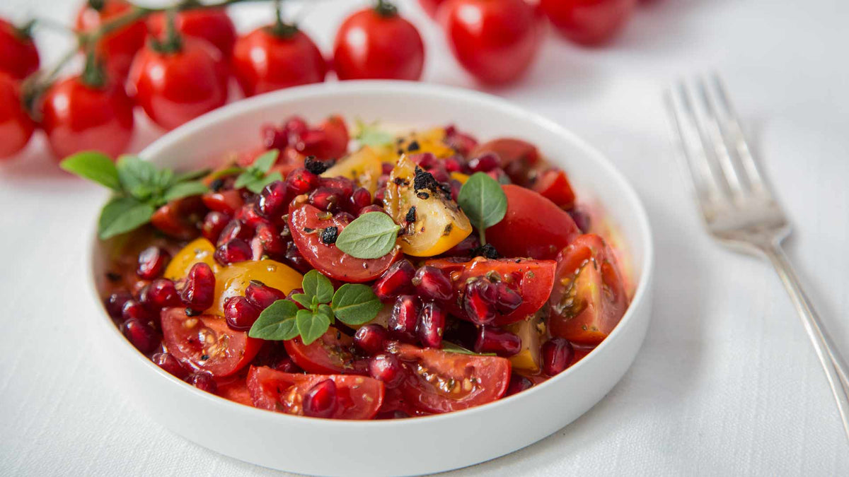 Ein weißer Schale Tomaten-Granatapfel-Salat mit Granatapfeldicksaft, garniert mit frischen Kräutern.