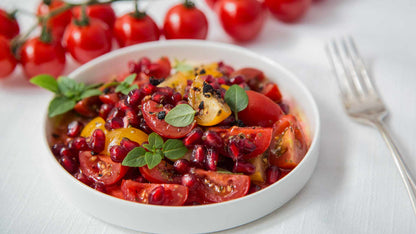 Ein weißer Schale Tomaten-Granatapfel-Salat mit Granatapfeldicksaft, garniert mit frischen Kräutern.