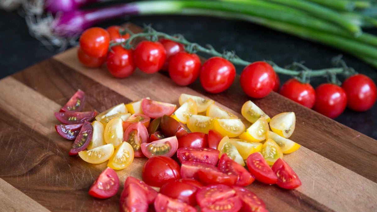 Bunte Kirschtomaten, ganz und in Scheiben geschnitten, mit Frühlingszwiebeln auf einem Holzbrett.