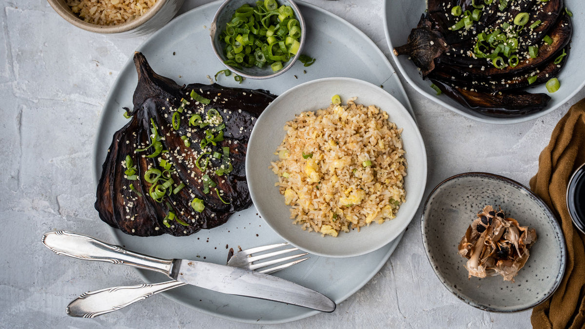 Gegrillte Aubergine, gebratener Reis und Frühlingszwiebeln auf grauen Tellern mit Knoblauchpaste.