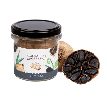 Glas mit Aufschrift Bio Schwarzer Knoblauch und eine ganze Knoblauchknolle daneben.