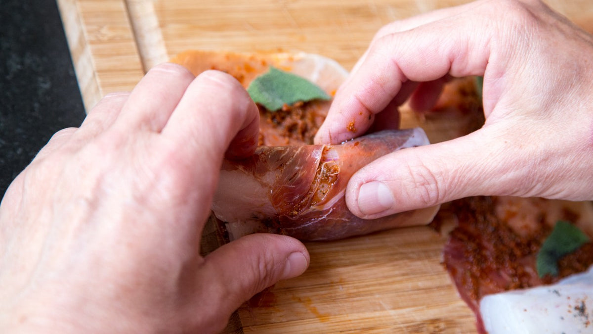 Hände rollen gewürztes Fleisch auf einem Holzbrett.