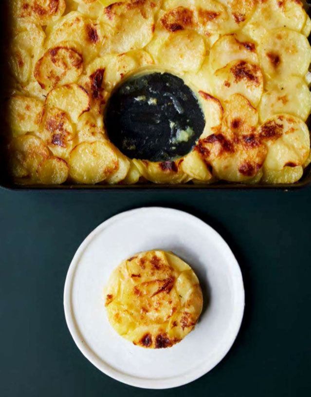 Kartoffelgratin in Auflaufform serviert, mit einem Stück auf einem Teller daneben.