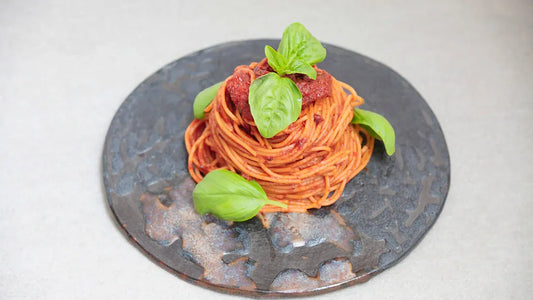 Spaghetti mit Tomatensauce, frischem Basilikum und Bio Gochujang auf dunklem Teller.