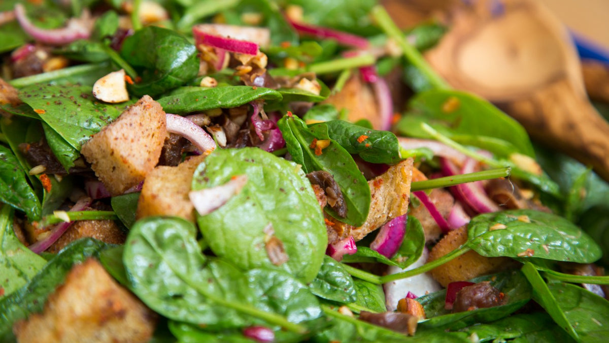 Nahaufnahme von Spinatsalat mit Croutons, roten Zwiebeln und knackigen Nüssen.