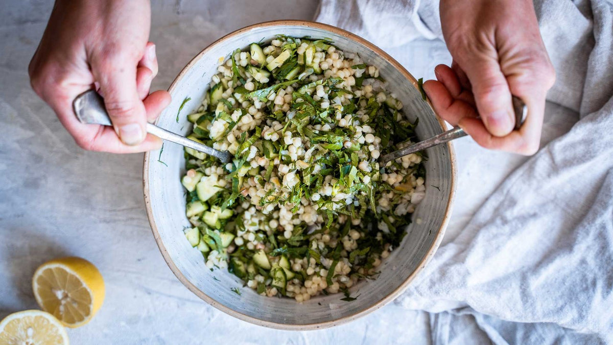 Mit den Händen den Perlcouscous-Salat mit frischen Kräutern, Gurke und Zitronenscheiben vermengen.