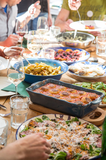 Salat und Lasagne werden von einer Gruppe an einem sonnigen Tisch mit Gewürzseminar Pfeffer geteilt.