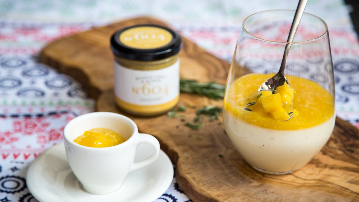 Ein Glas und eine Tasse mit cremigem Dessert und Mangosauce auf einem Holzbrett.