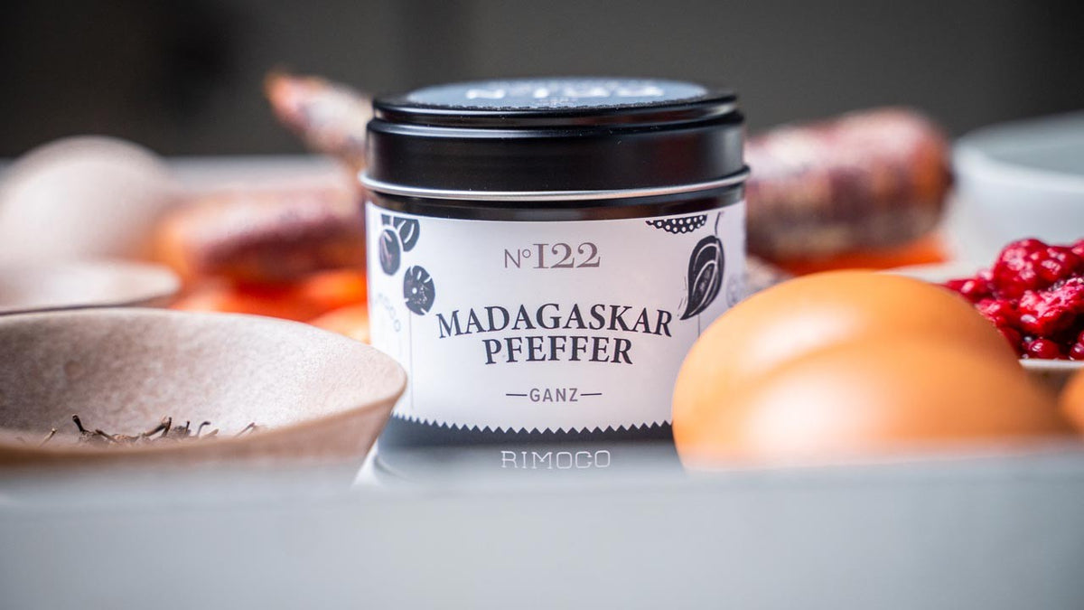Eine Dose Madagaskar-Pfeffer steht auf einem Tisch zwischen Eiern, Gewürzen und roten Beeren.