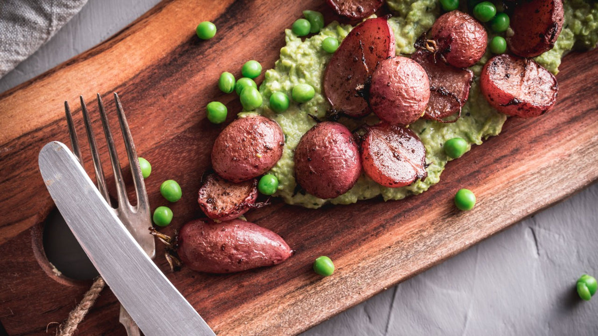 Gegrillte rote Kartoffeln auf Erbsenpüree mit grünen Erbsen, serviert mit Gabel und Messer.