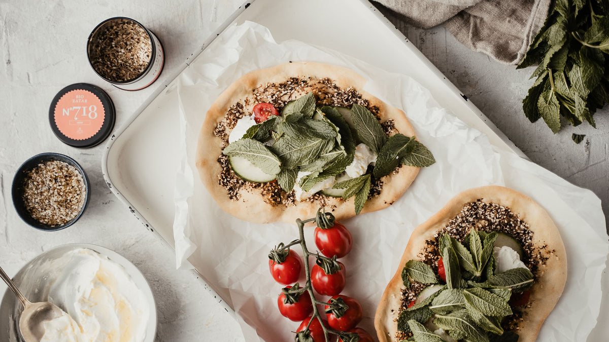 Fladenbrote mit Kräutern und Gemüse, dazu Tomaten und Gewürze. Gewürzset Ottolenghi sichtbar.