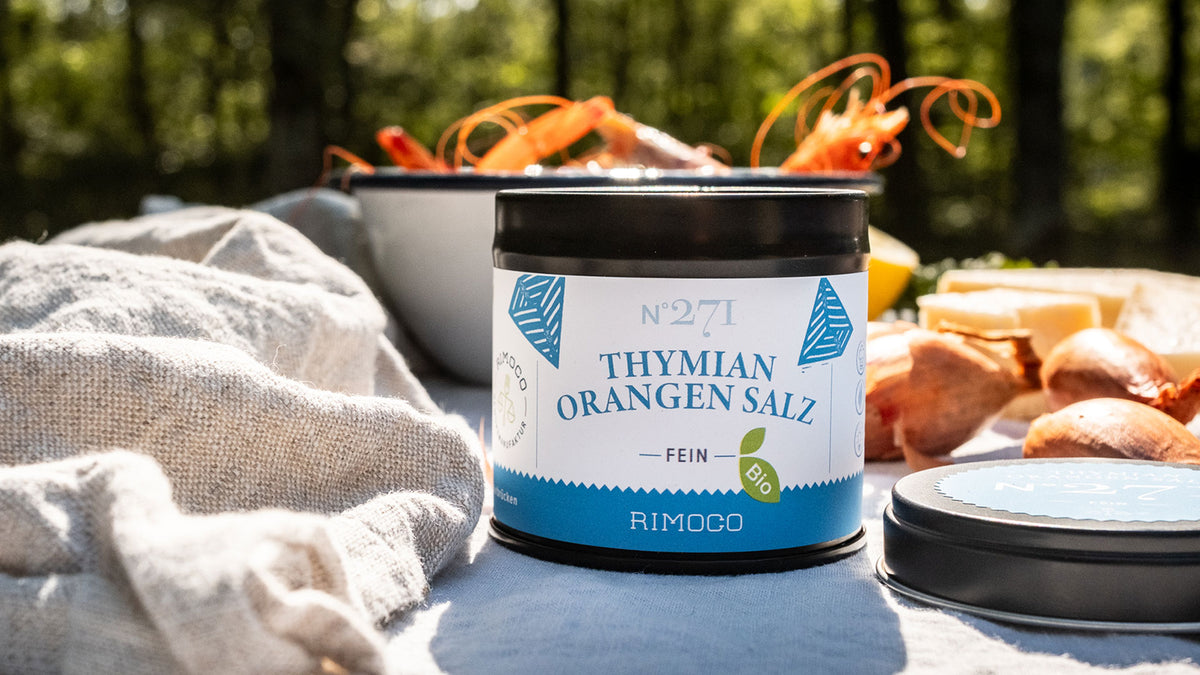 Rimoco Thymian-Orangen-Salz-Dose im Freien, daneben etwas Essen im Sonnenlicht.